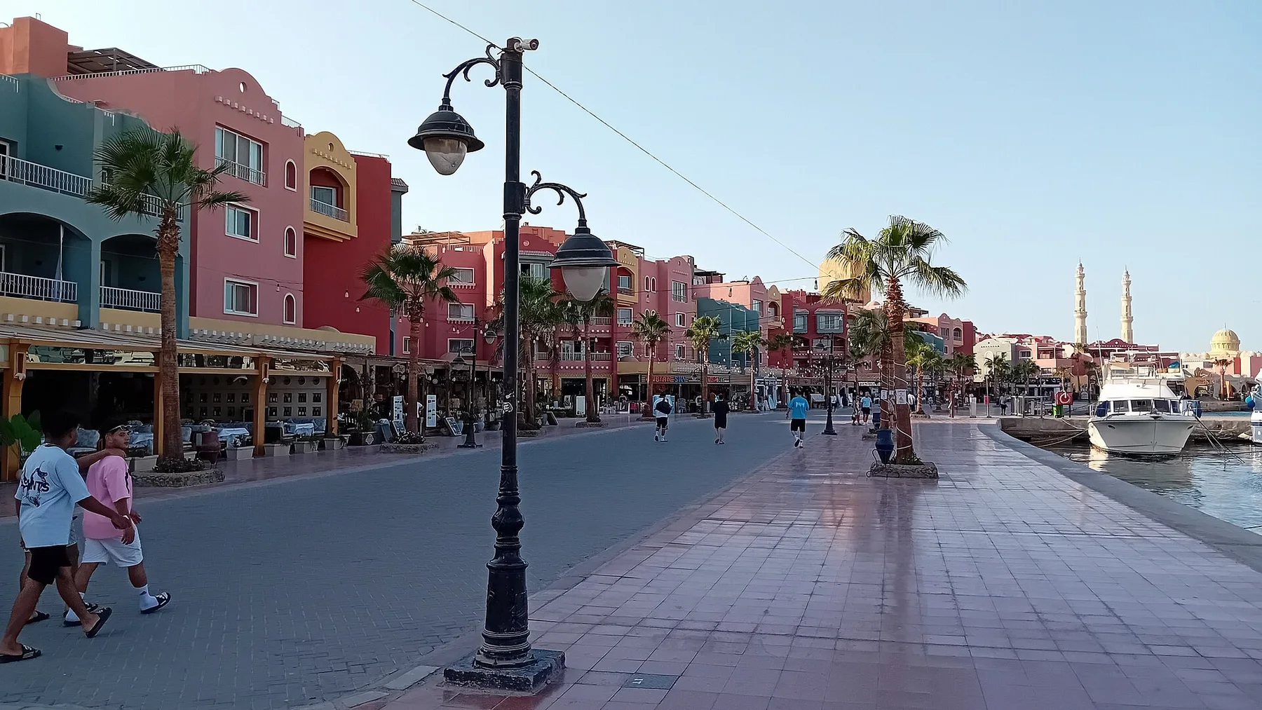 Promenade de la marina d’Hurghada bordée de façades colorées, de palmiers et de bateaux.