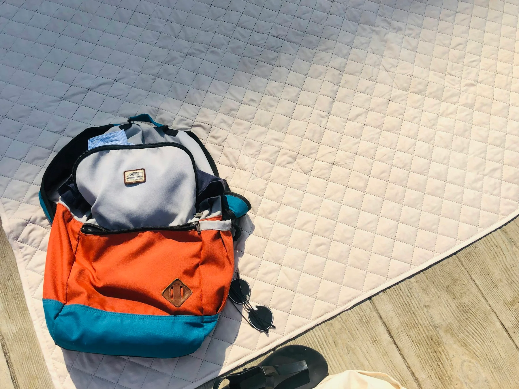 Sac orange et accessoires disposés sur un tissu clair.